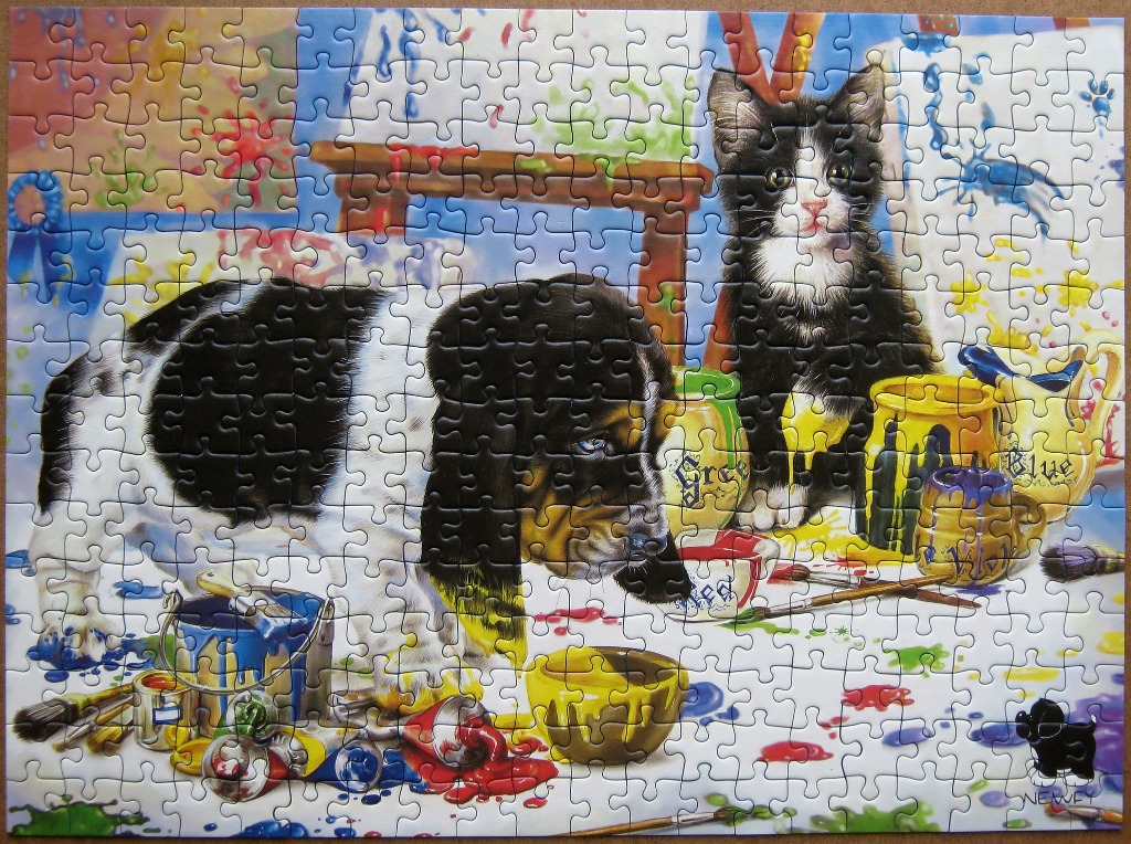 A black and white puppy and kitten sitting in a messy art studio with spilled paint.