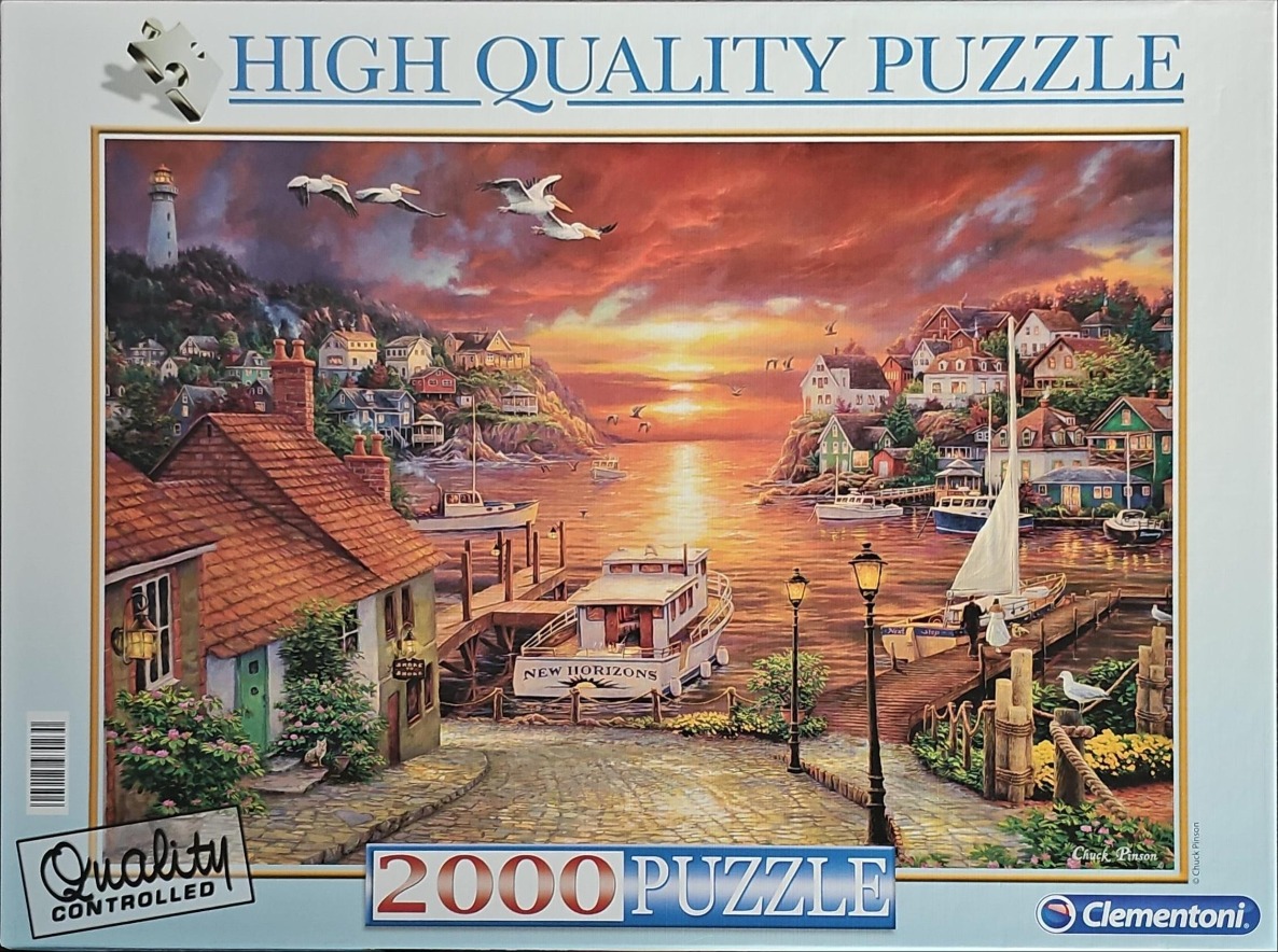 Coastal harbor scene at sunset with boats, a lighthouse, and seaside cottages.