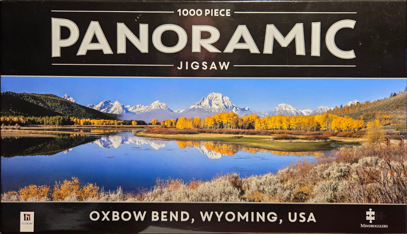 A panoramic landscape photo of Oxbow Bend in Wyoming during autumn, featuring snowy mountains reflected in a river.