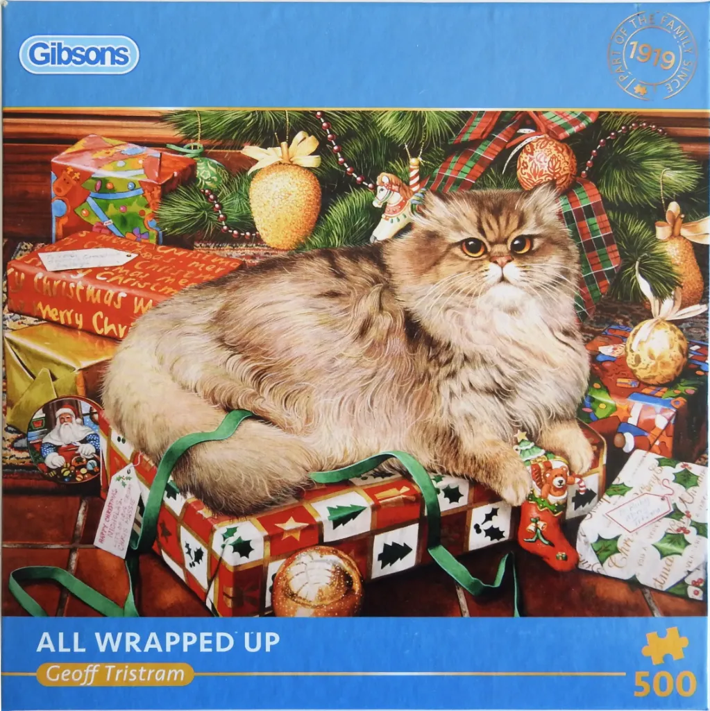 A long-haired, fluffy brown cat lounging on top of brightly wrapped Christmas gifts beneath a pine tree.