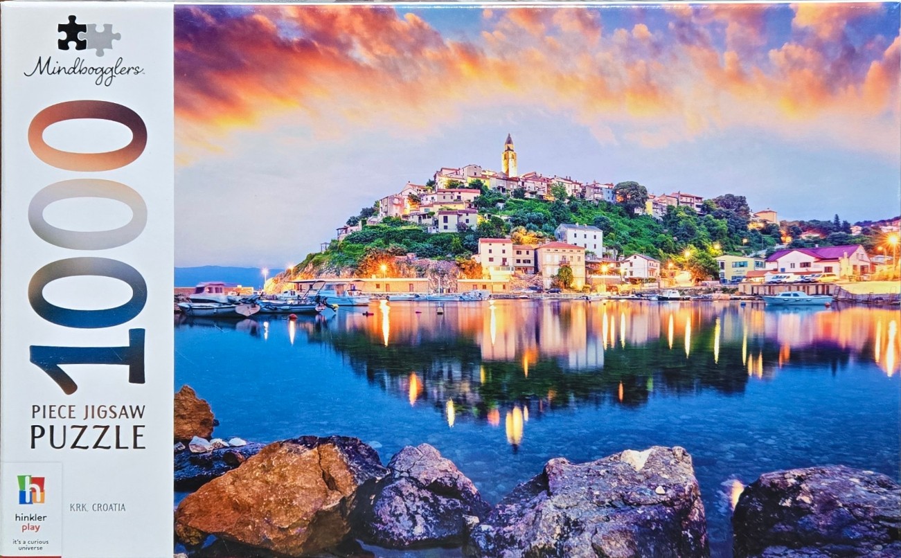 A scenic coastal village in Krk, Croatia, reflected in calm water at sunset with a dramatic orange and purple sky.