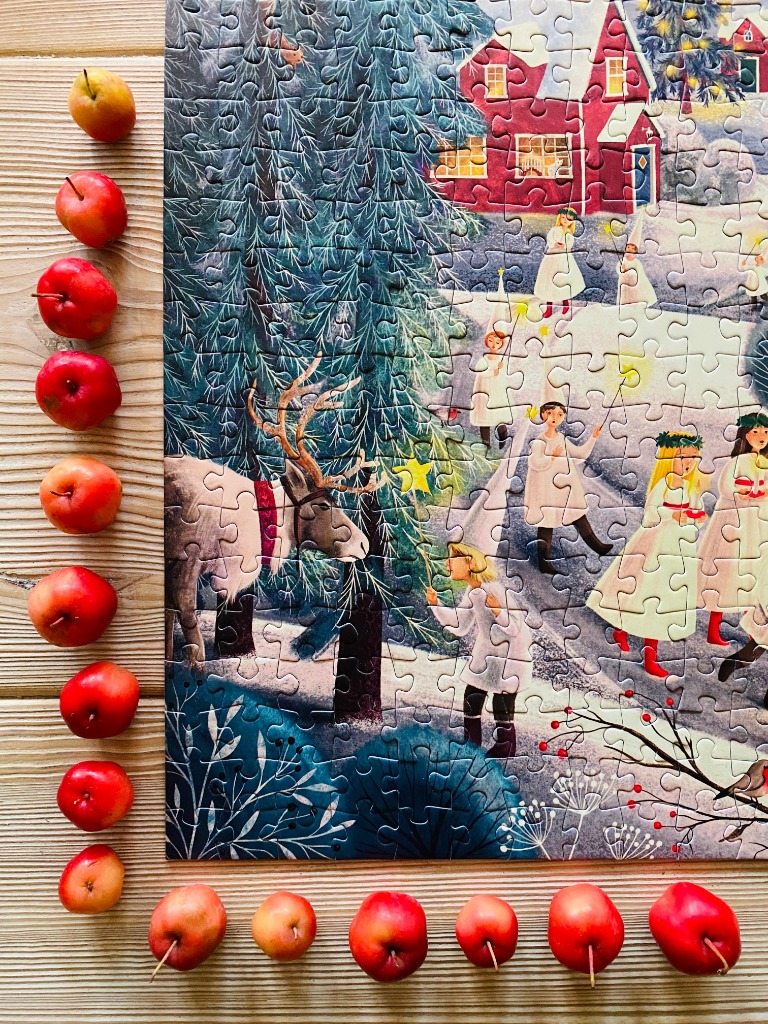 A festive winter scene with St. Lucia procession characters, a reindeer, and a red house, surrounded by fresh apples.