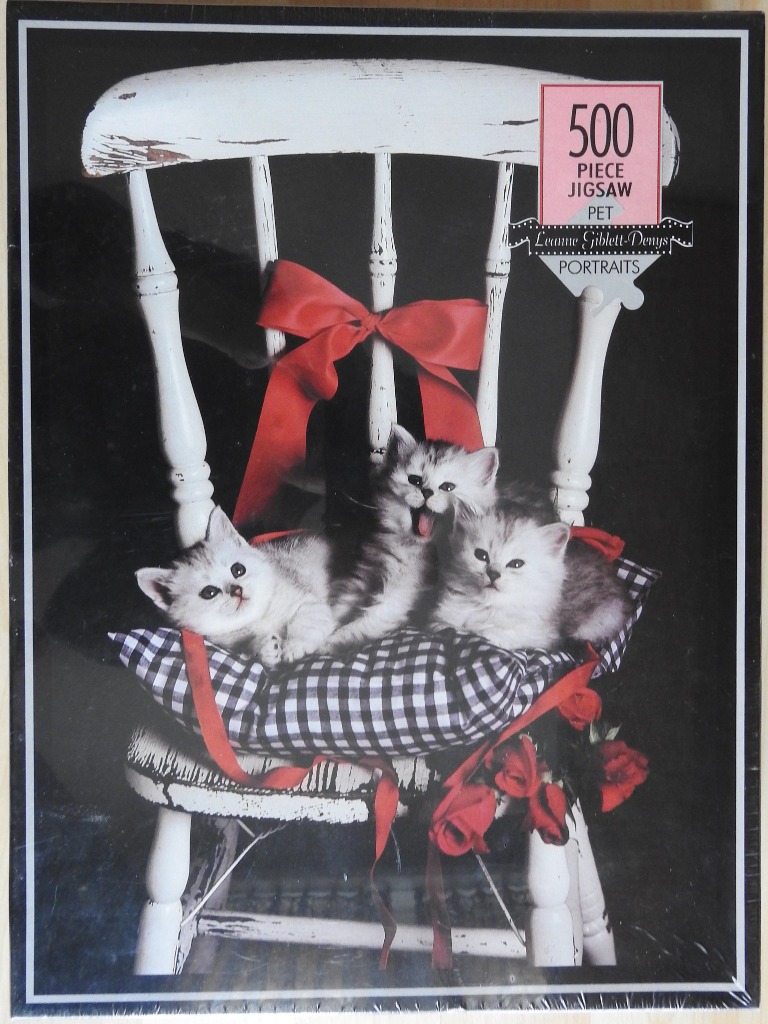 Three fluffy kittens sitting on a black-and-white gingham cushion on a vintage white chair.