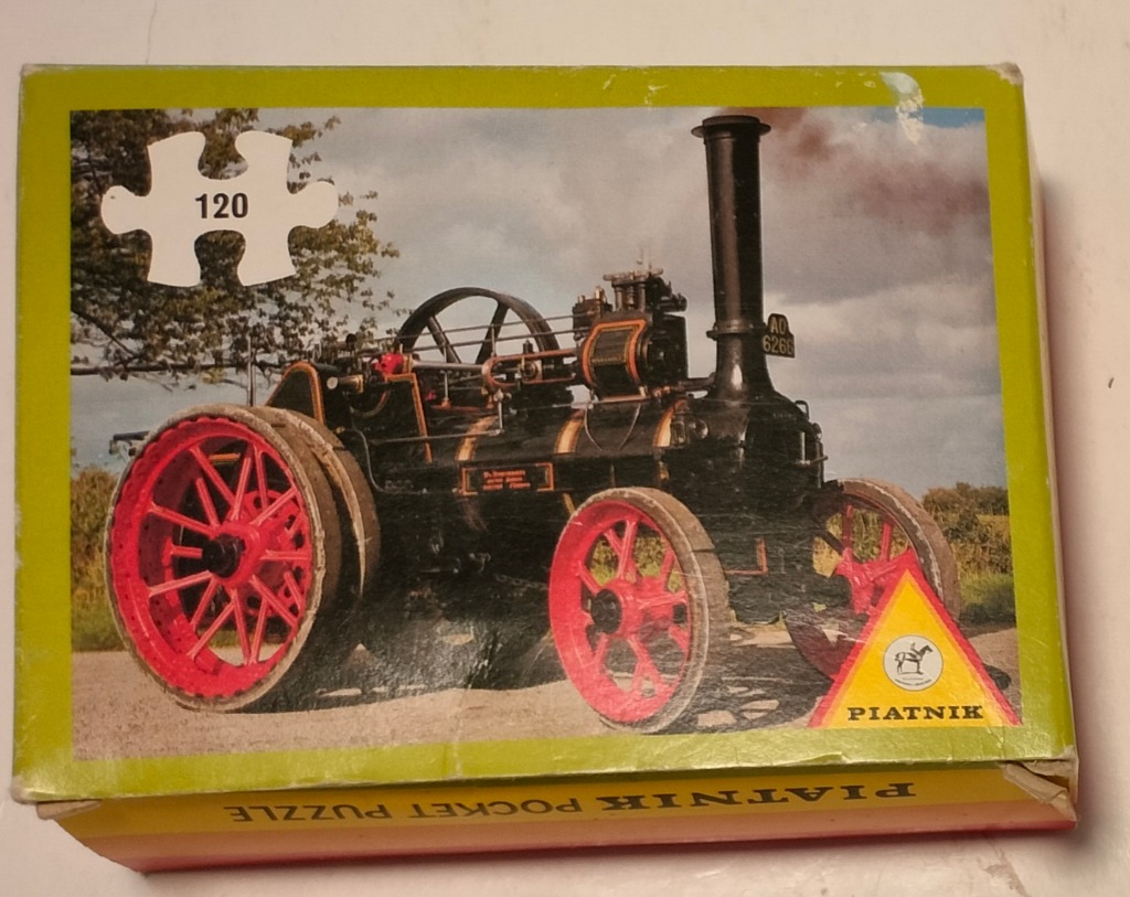 Antique black steam traction engine with vibrant red wheels parked on a dirt road against a cloudy sky.
