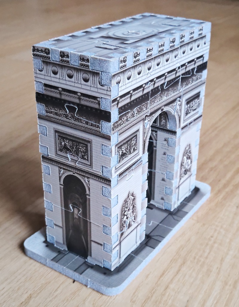 A three-dimensional architectural model of the Arc de Triomphe standing on a light wooden surface.