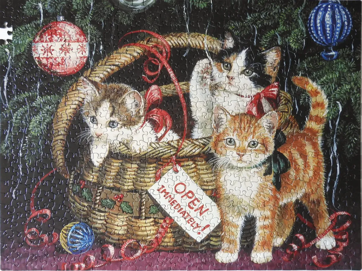 Three kittens sitting in and around a wicker basket under a Christmas tree
