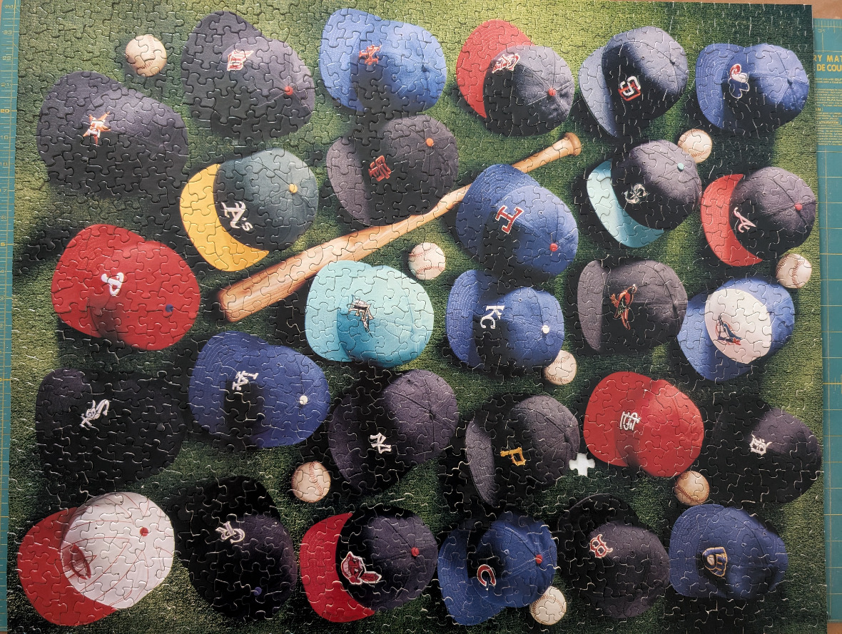 A collection of Major League Baseball caps and a wooden bat scattered on a grassy field.