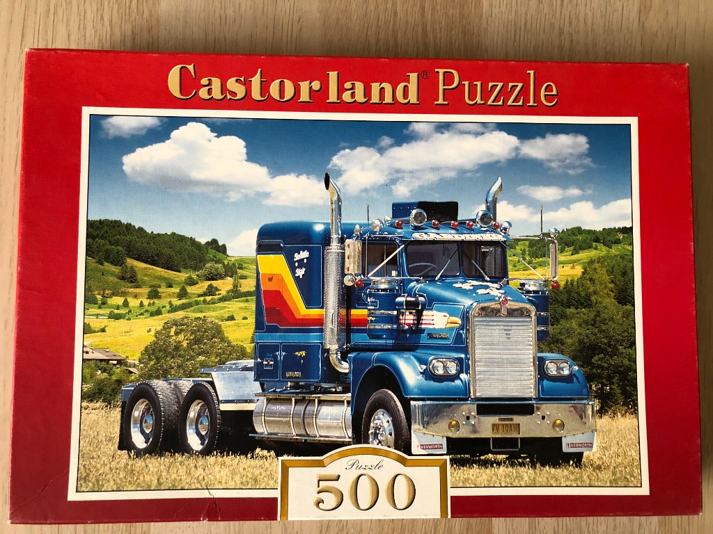 A blue semi-truck parked in a rural field with rolling green hills in the background.