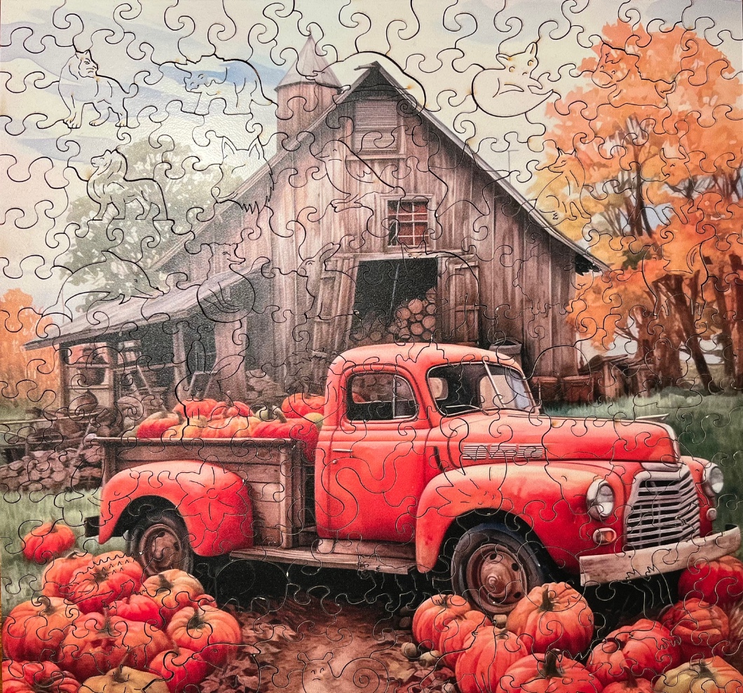 A vintage red pickup truck filled with pumpkins parked in front of a rustic wooden barn in autumn.