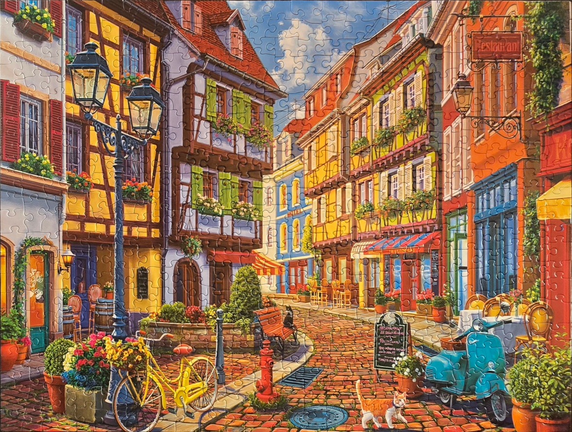 A vibrant, sunny street scene in a European village with colorful half-timbered buildings, a yellow bicycle, and a scooter.