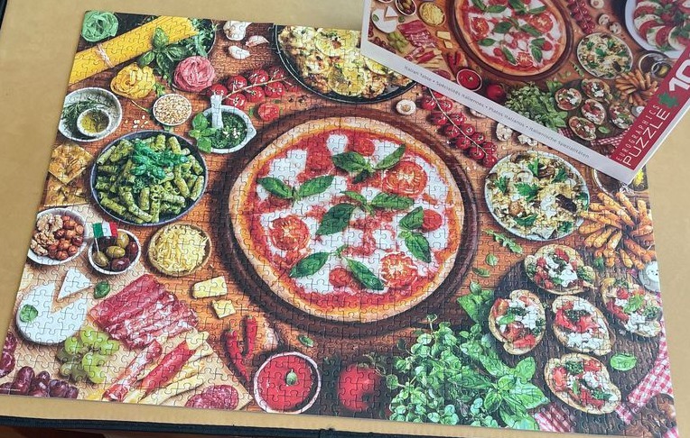 A top-down view of an abundant Italian feast featuring a central margherita pizza surrounded by pasta, antipasti, and herbs.