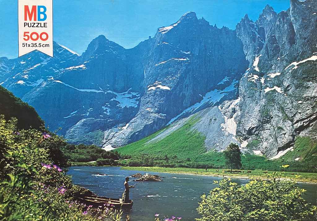 A lone fisherman in a small wooden boat on a river beneath towering, snow-dusted mountain peaks.
