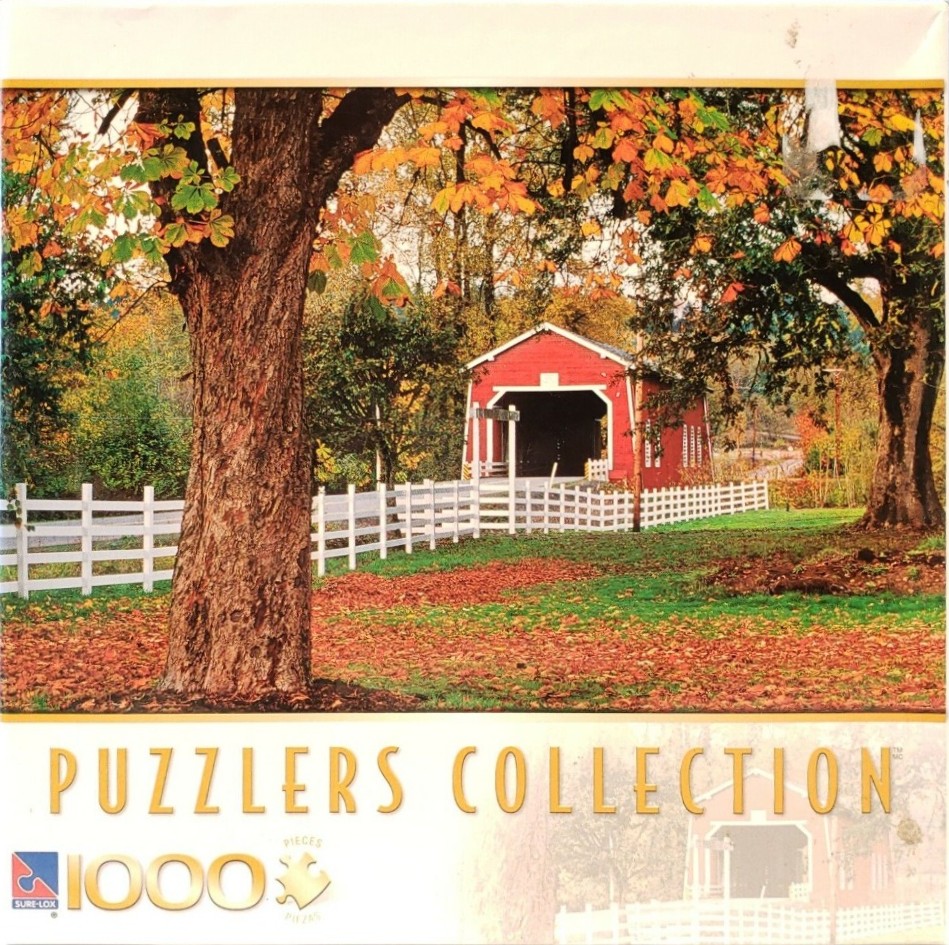 A red covered bridge surrounded by autumn trees and a white picket fence.