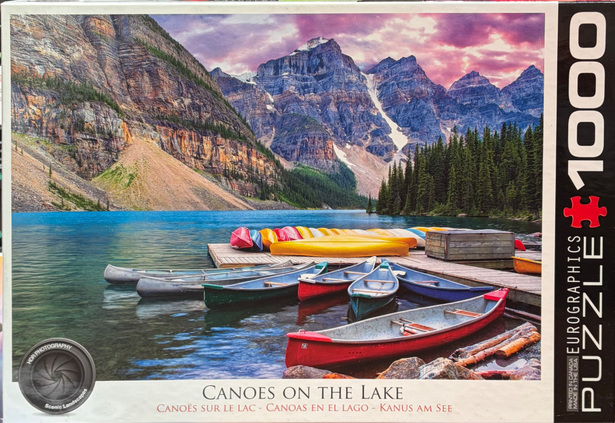 A row of colorful canoes docked at a wooden pier in front of a majestic mountain range at sunset.