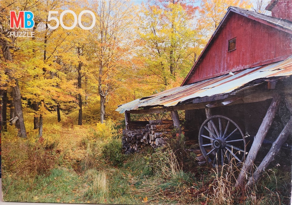An old red barn with a large wagon wheel in a forest during autumn.