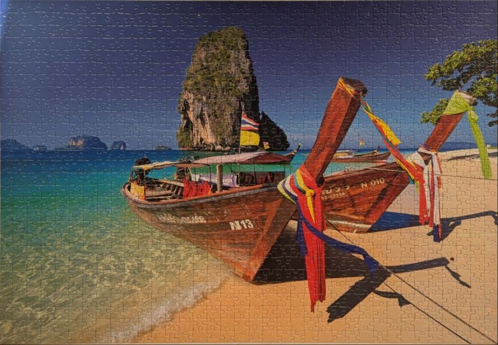 Two traditional wooden longtail boats resting on a tropical beach in Thailand with a limestone karst in the background.
