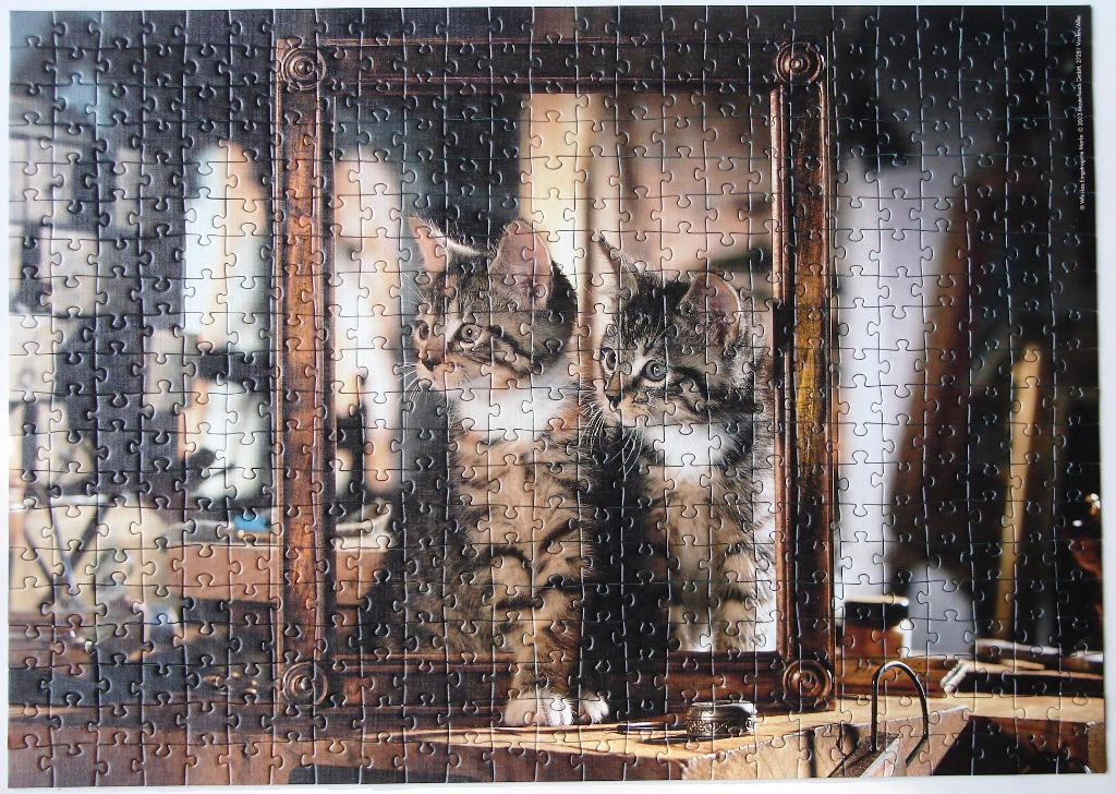 Two tabby kittens sitting in a dark, ornate wooden frame in a workshop setting.