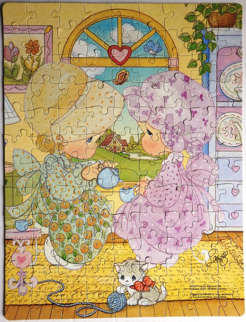 Two young girls in bonnets having a tea party with a kitten on a rug