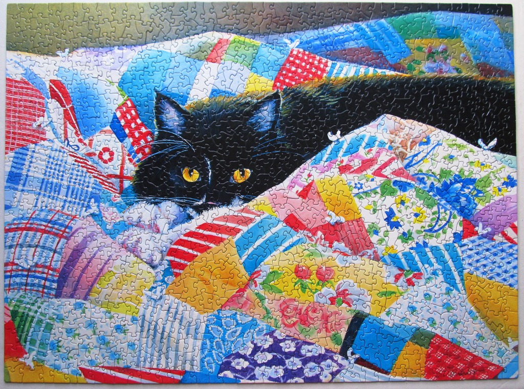 A black cat with golden eyes resting on a vibrant, colorful patchwork quilt.