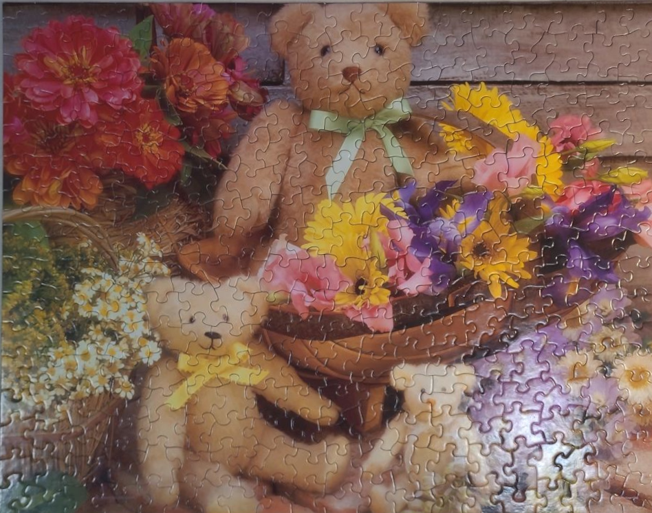 Three teddy bears sitting amidst baskets of vibrant colorful flowers against a rustic wooden background.