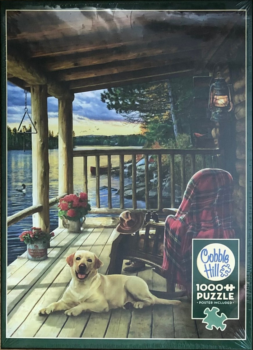 A yellow Labrador lies on a wooden cabin porch overlooking a tranquil lake at twilight.