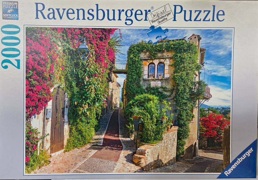 A narrow cobblestone street in a Mediterranean village lined with stone buildings covered in vibrant bougainvillea.