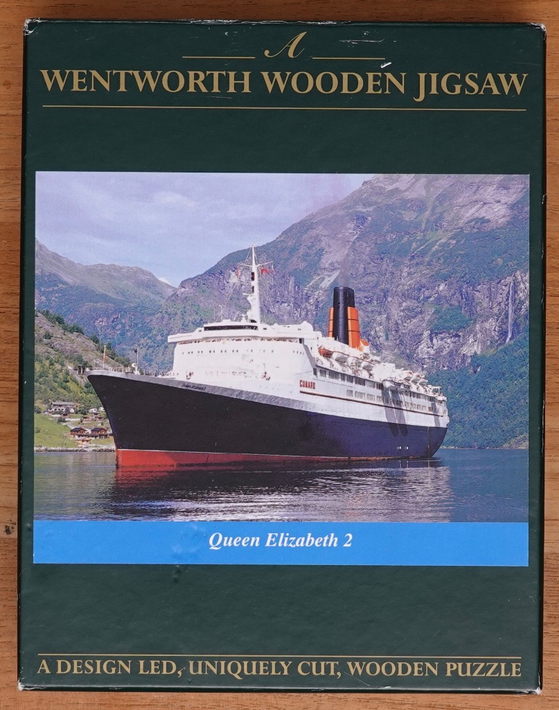 The Queen Elizabeth 2 ocean liner sailing through a mountainous fjord landscape.