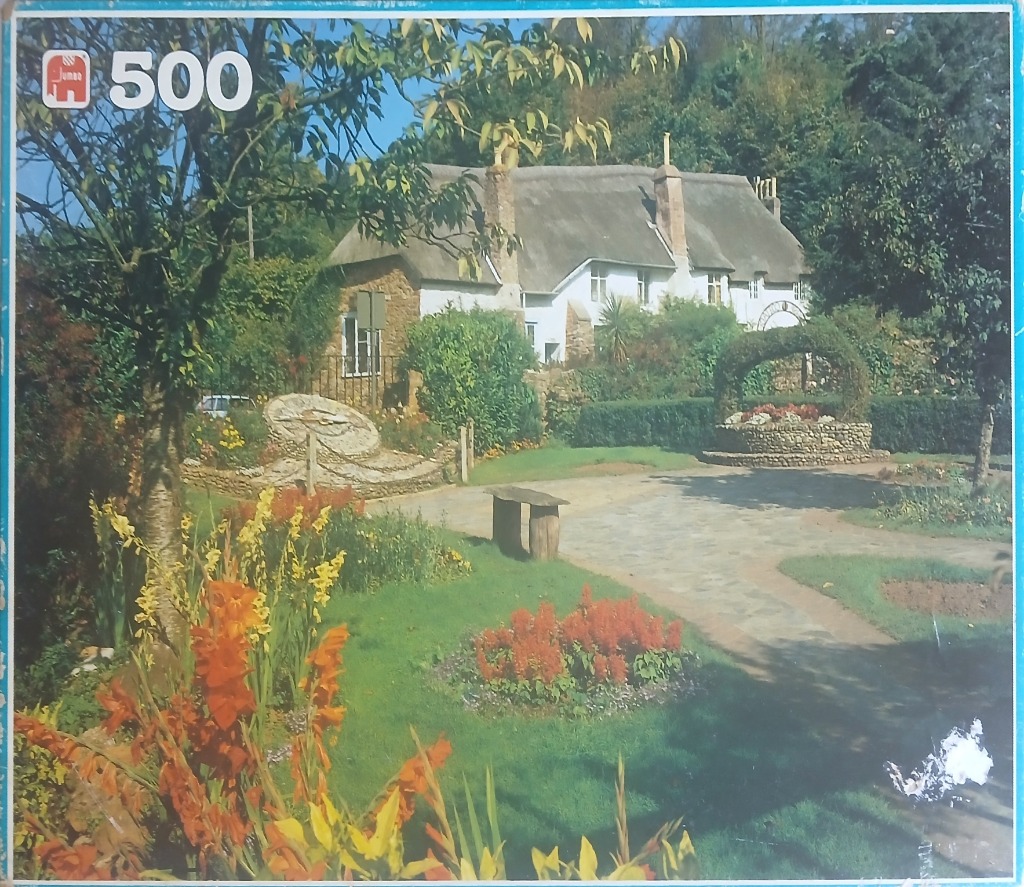A sunny garden scene featuring a white thatched cottage, stone pathways, and vibrant red and yellow flowers.