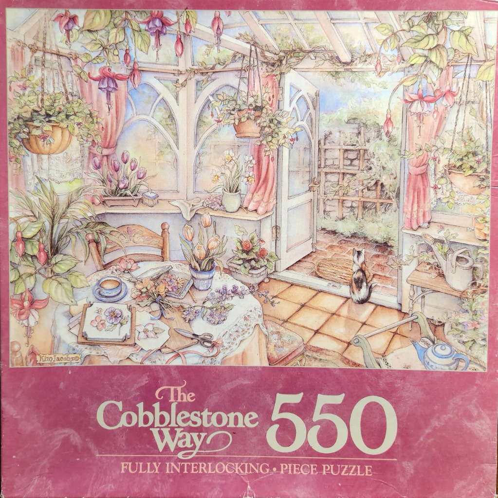 A sunlit conservatory filled with hanging fuchsia plants, a tea table, and a calico cat sitting by an open door.