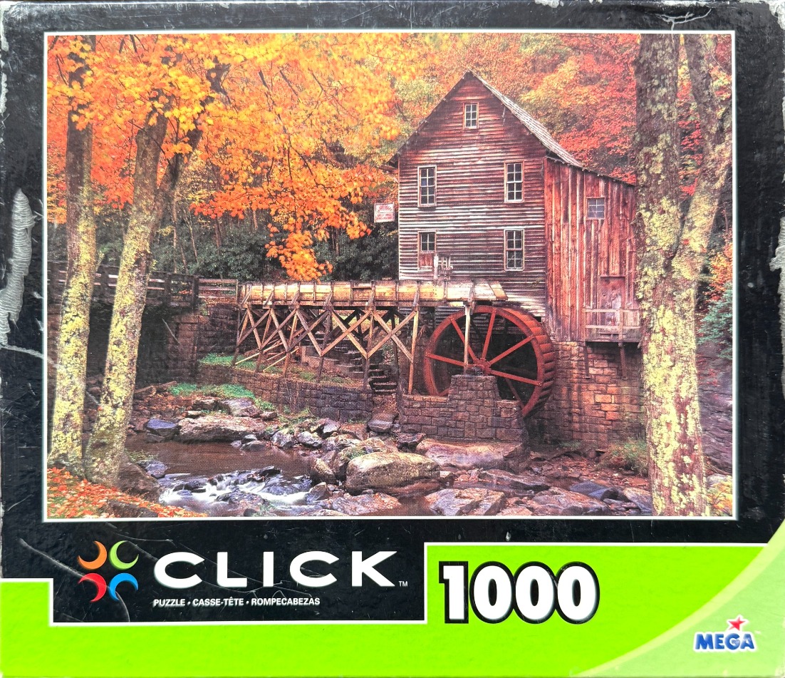 An old wooden grist mill with a red water wheel set in a forest during autumn foliage.