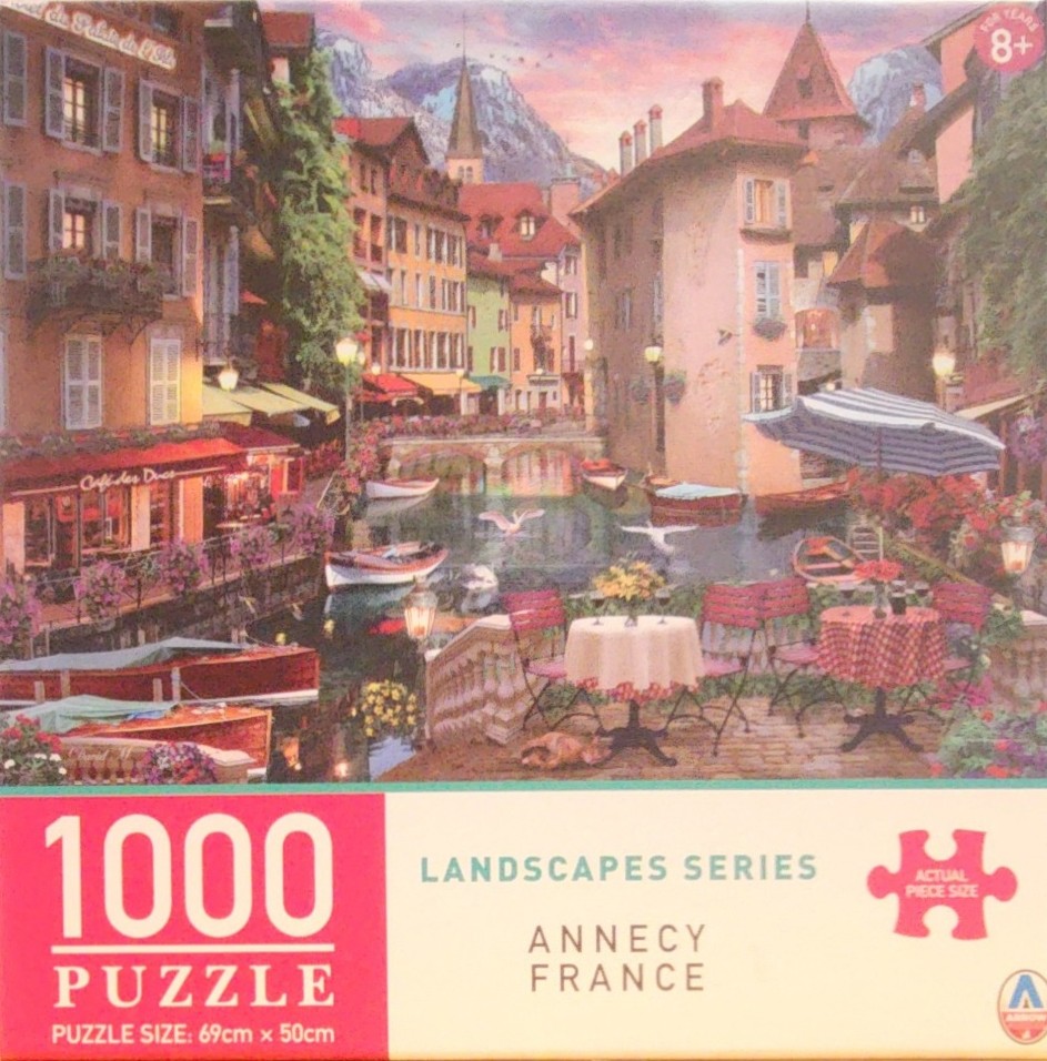 A peaceful canal scene in Annecy, France, featuring waterfront cafes, small boats, and old European architecture.