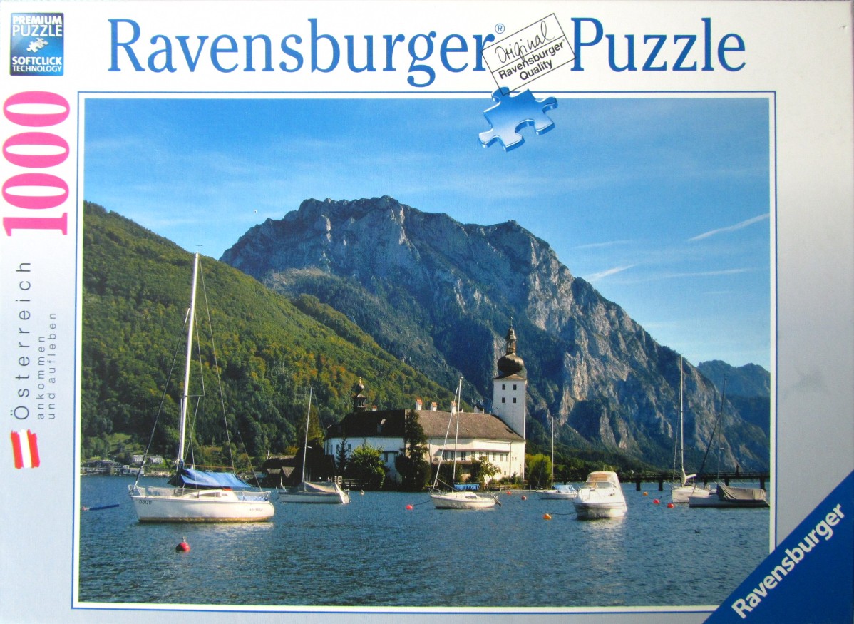 A photograph of Schloss Ort castle on Traunsee lake in Austria, surrounded by mountains and sailing boats.