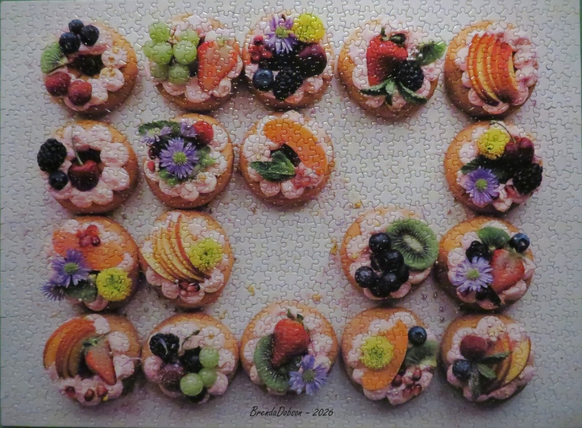 A rectangular grid of seventeen decorated round cookies topped with fresh fruit and edible flowers.