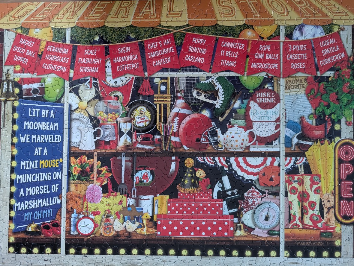 A whimsical store display window filled with a cluttered collection of mismatched objects and wordplay banners.