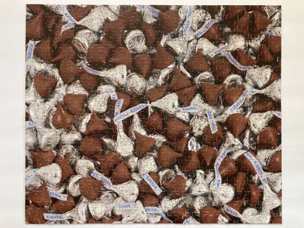 A close-up view of numerous chocolate candies wrapped in silver foil, scattered together to fill the frame.