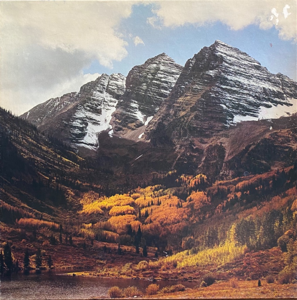 Snow-capped mountain peaks towering over an autumn valley with golden aspens and a reflecting lake.