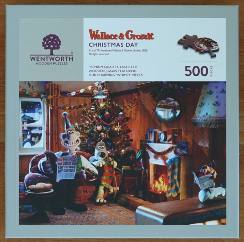 Wallace and Gromit sitting in a cozy living room by a Christmas tree and fireplace.