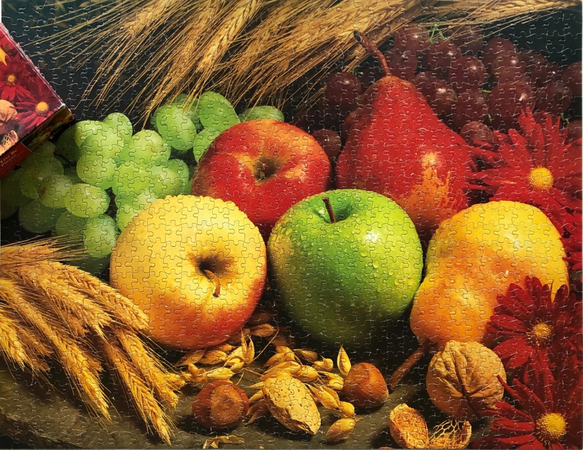 A still life arrangement of fruits, wheat, nuts, and red flowers.