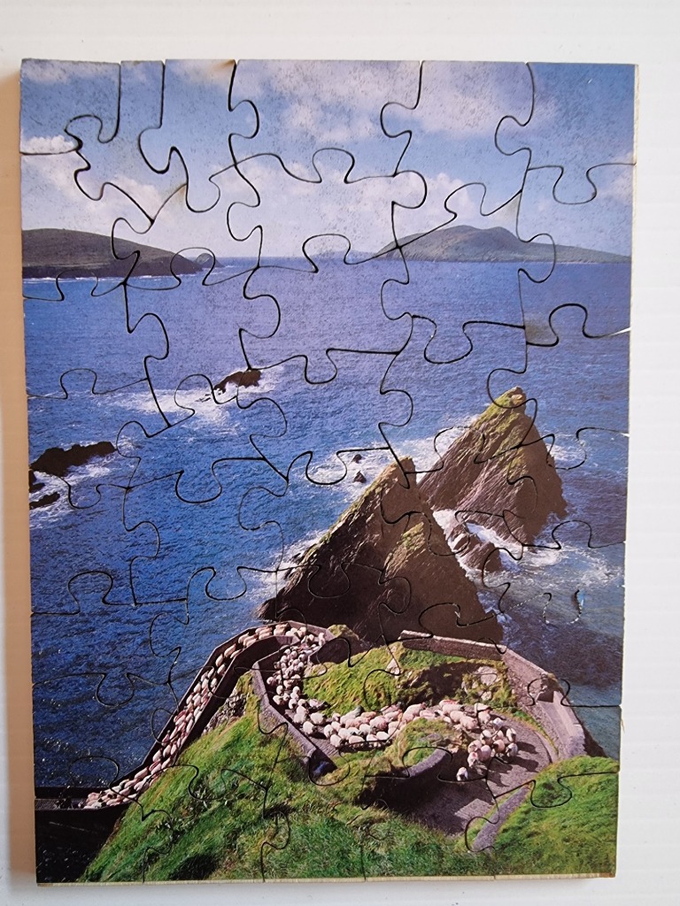 A flock of sheep walking along a coastal cliff path overlooking the blue sea and rocky islands.