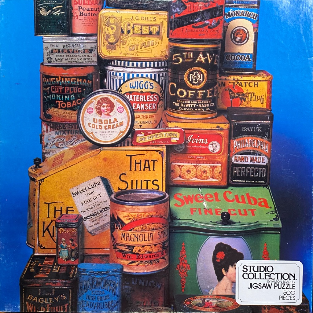 A still life of vintage advertising tins and containers arranged in a colorful stack against a bright blue background.