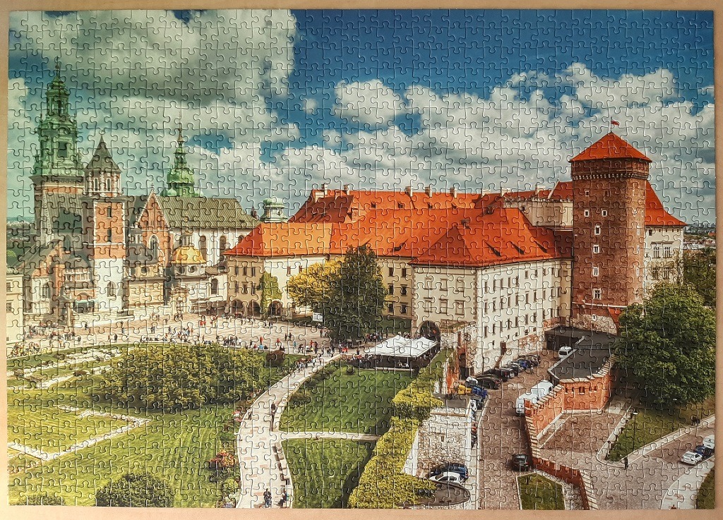 A panoramic view of Wawel Royal Castle in Krakow, Poland, under a bright, cloudy blue sky.