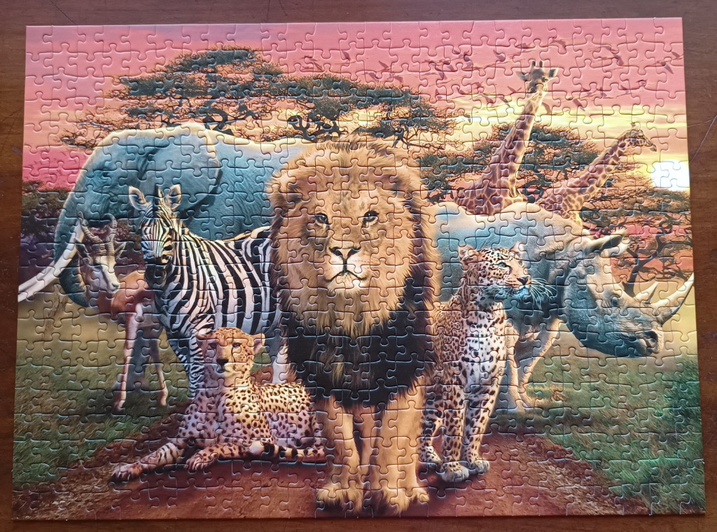 A group of African savanna animals including a lion, zebra, cheetah, elephant, and giraffe at sunset.