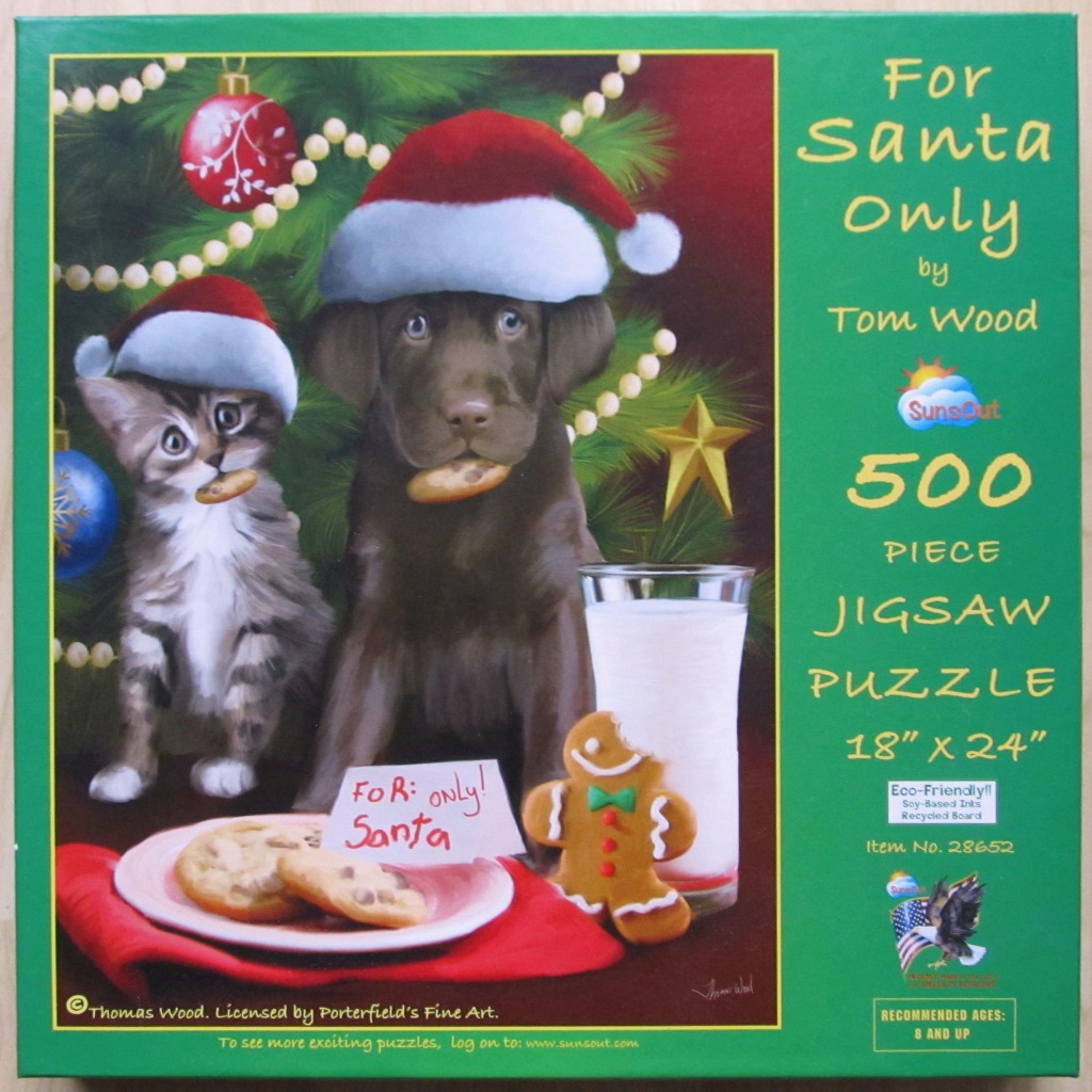 A puppy and kitten wearing Santa hats sitting in front of a Christmas tree with cookies and milk.
