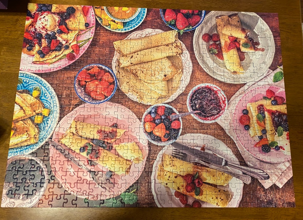 A top-down view of a rustic breakfast table filled with plates of crepes, berries, and bowls of fruit preserves.