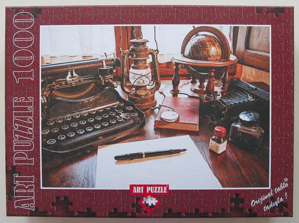 Still life photograph of antique writing tools, a vintage typewriter, a lantern, and a globe on a wooden desk.