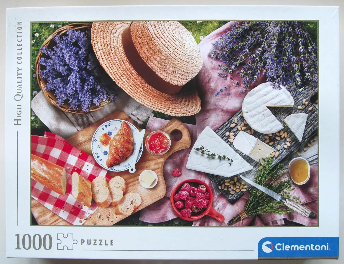 An overhead picnic scene featuring a straw hat, lavender, cheeses, fresh bread, and berries on a pink linen cloth.