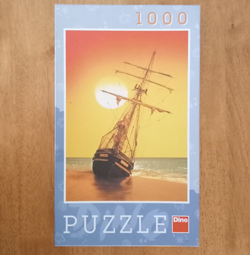 A tall ship grounded on a sandy beach at sunset against a yellow and orange gradient sky.