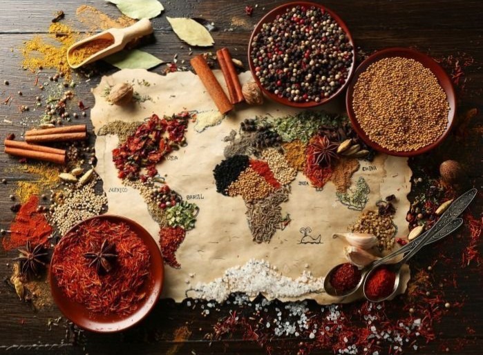 A world map formed by various colorful spices on aged paper against a dark wooden surface.