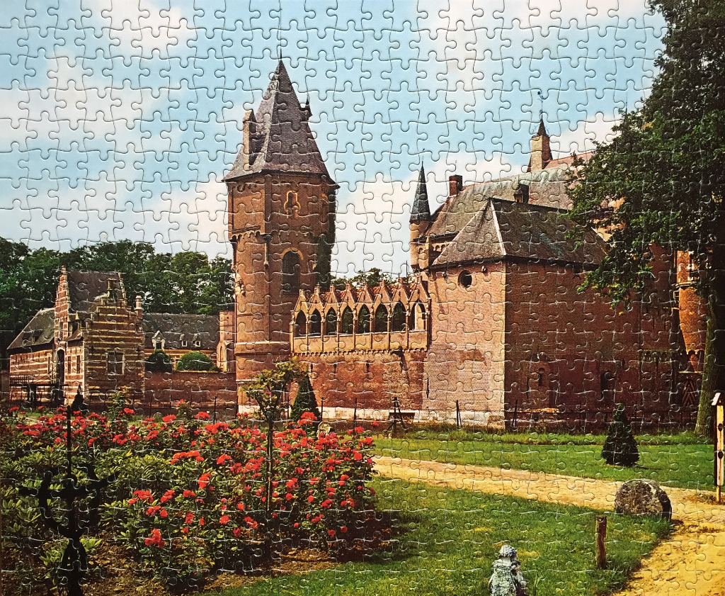 A view of a historic brick castle with a rose garden in the foreground under a blue sky.