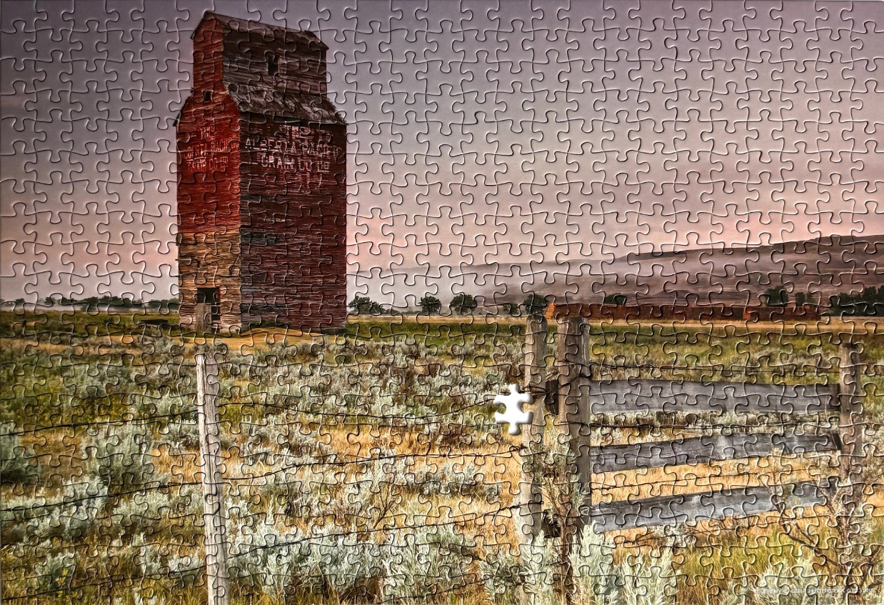 A vintage wooden grain elevator standing in a quiet rural field at dusk.